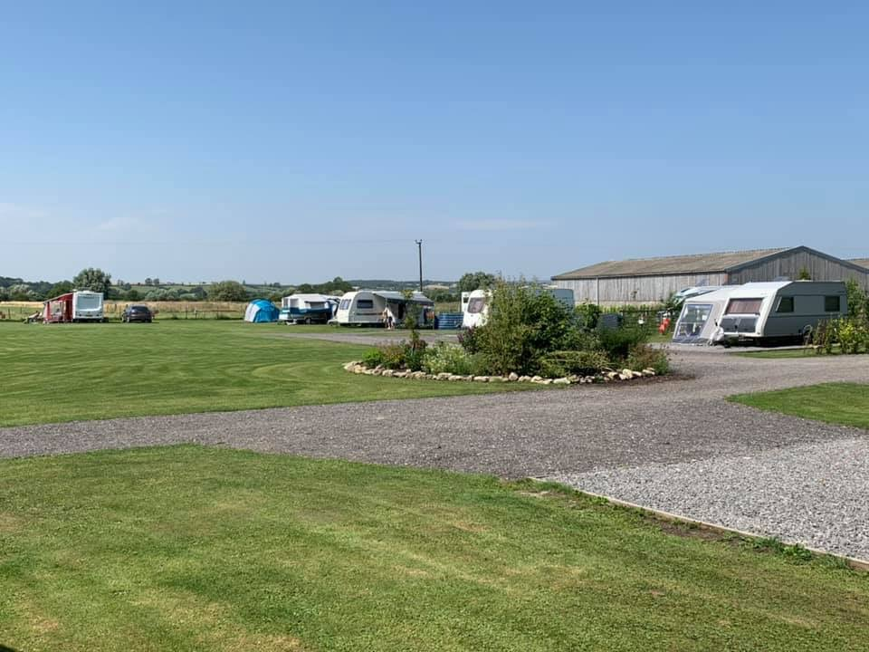 View of caravan park with caravans on the pitches and a farm building in the background