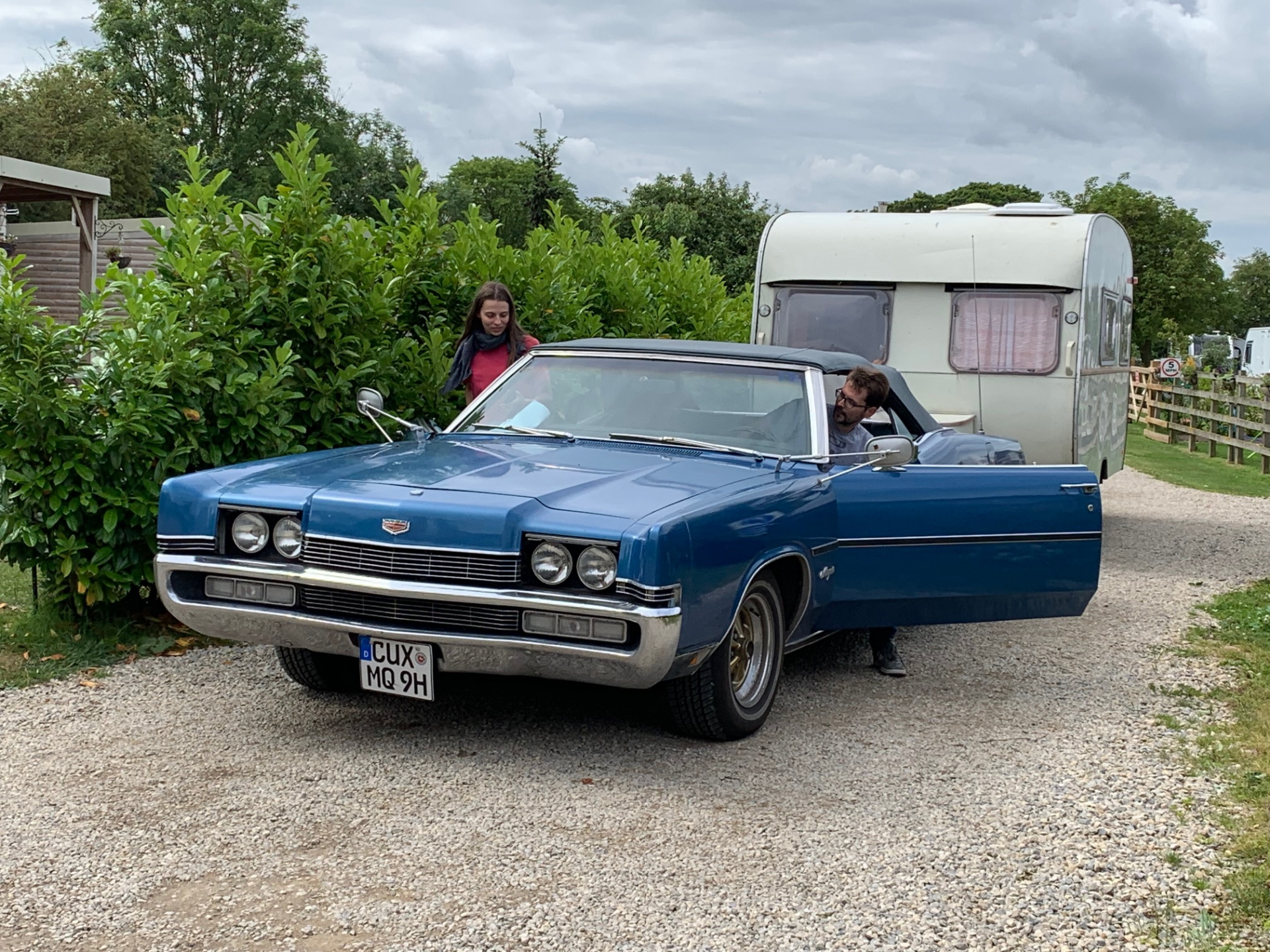 Young couple with a Classic, blue american car pulling a white caravan.