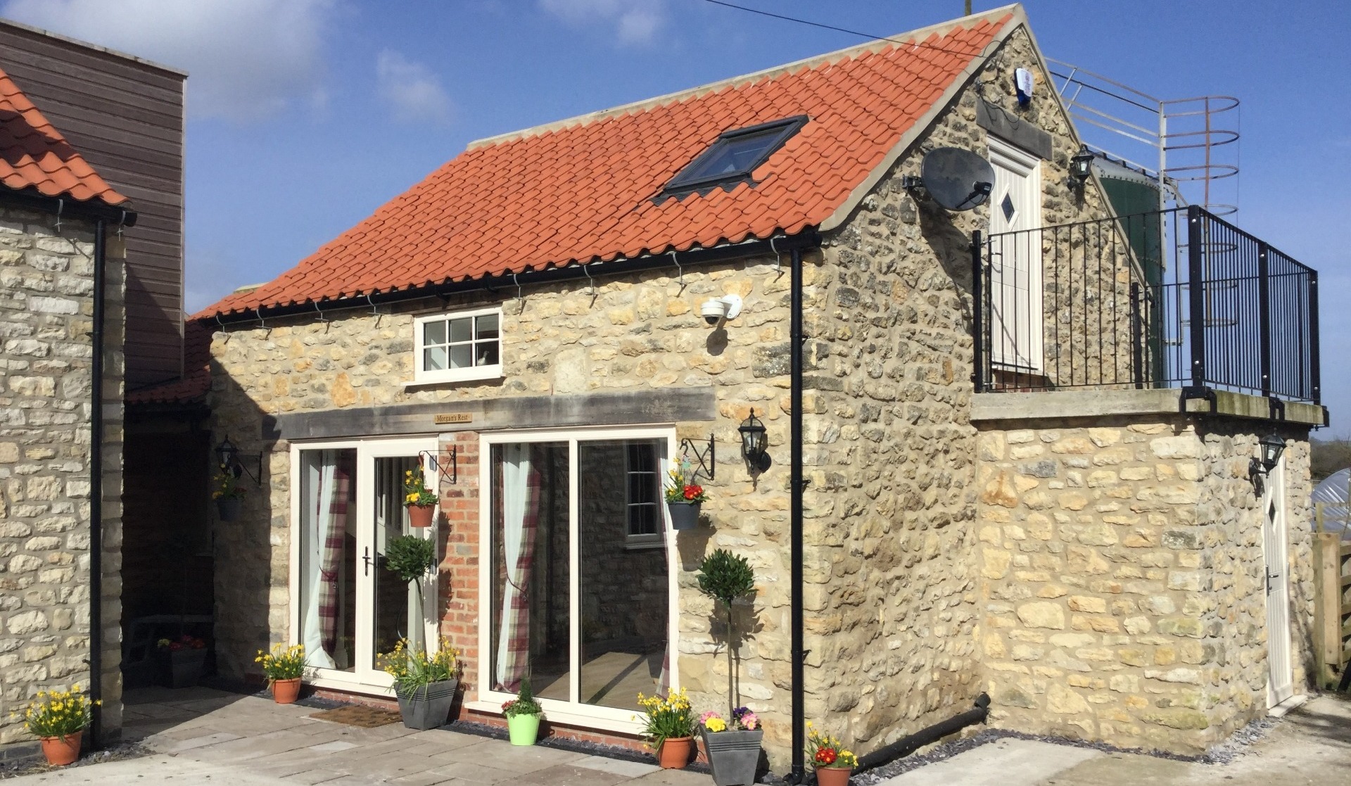 Ston holiday cottage with two sets of patio doors, a small window above and a red tiled roof with velux window. Beige upstairs door with balcony and black railings